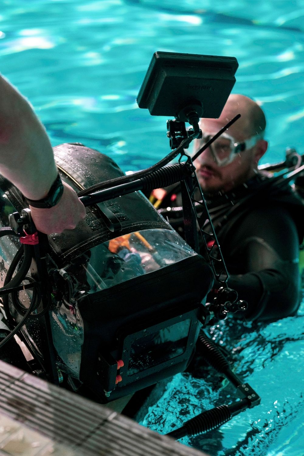 Diver operating underwater camera housing in pool